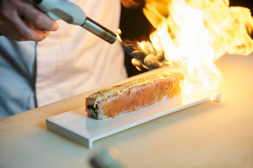 Chef prepares sushi with torch burner. Classic Japanese sushi food served on a stone plate - Powered by Adobe