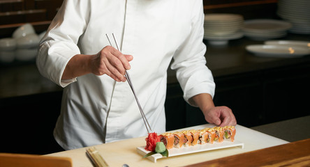 Chef prepares sushi with torch burner. Classic Japanese sushi food served on a stone plate