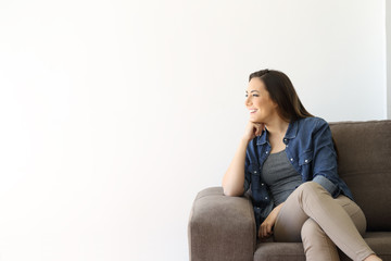 Obraz premium Happy single woman looking at side sitting on a sofa
