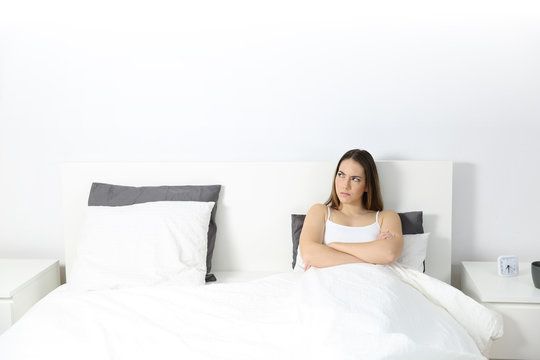Angry woman sitting on the bed looking at side