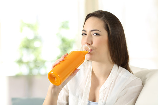 Woman drinking orange juice from a bottle looking at you
