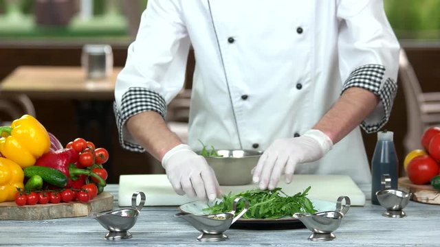Chef preparing ingredient for salad. Fresh arugula on the plate.