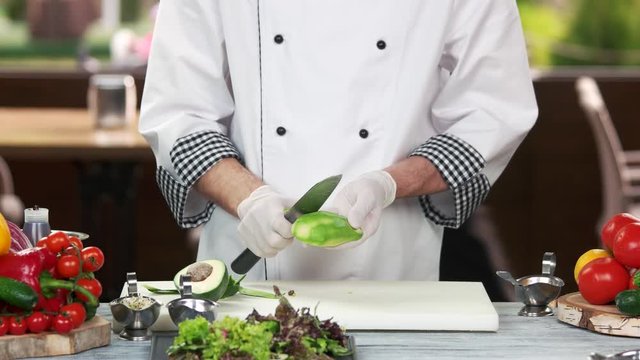 Chef with knife peeling avocado. Fresh tropical fruit.