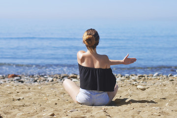 Young woman makes meditation in lotus pose on sea / ocean beach, harmony and contemplation. Beautiful girl practicing yoga at sea resort at her vacation. Life style.