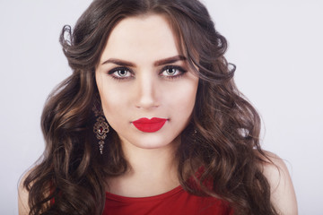 Fototapeta premium Beautiful luxury woman with jewelry, earrings. Beauty and accessories. Sexy brunette girl with big red lips in a white dress. Fashion model with long curly hair on red background. Smokeys eyes make up