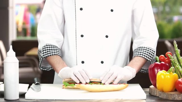 Hands of chef preparing sandwich. Bun, vegetables and sausage.