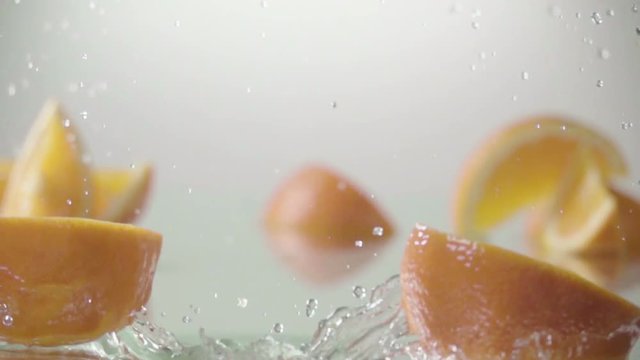 Orange hits orange juice surface and splits into halves. Slow motion shot