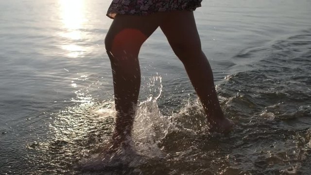 Low-section shot of legs of unrecognizable woman in floral dress walking in lake on summer evening