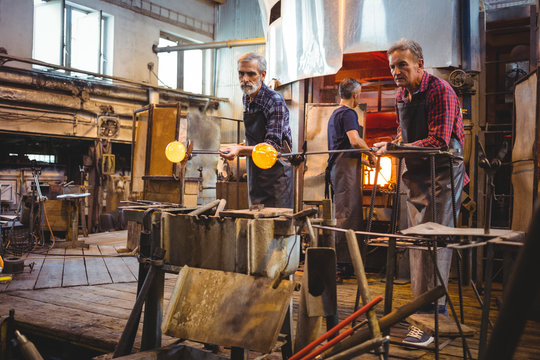Team of glassblowers shaping a glass on the blowpipe