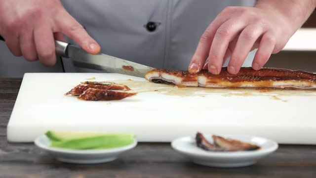 Male hands slicing fish. Smoked eel, sushi ingredient.