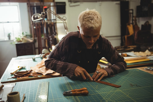 Attentive craftswoman cutting a piece of leather