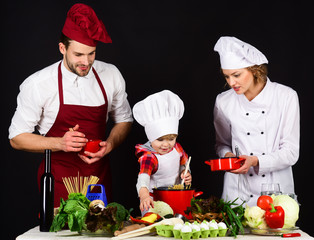 Happy family in kitchen. Healthy food at home. Adorable kid in chef hat. Preparation to dinner. Parents with child preparing dinner. Cheerful parents teaching a boy how to cook.