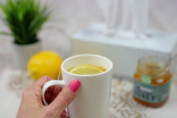 Cup of hot tea with honey and lemons, tissues on table, cold flu concept