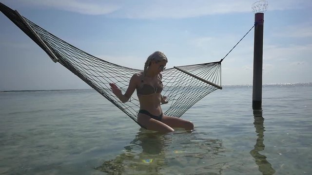 Trendy young woman in a bikini poses while sitting in a hammock in the sea