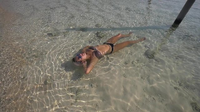 Young female traveler in a bikini floats in shallow sea in a beautiful afternoon
