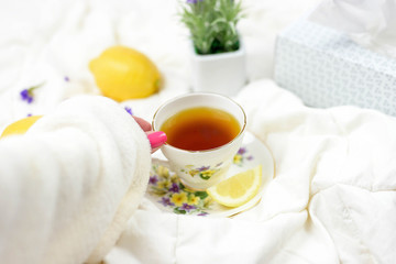 Woman's hand with cup of tea in bed