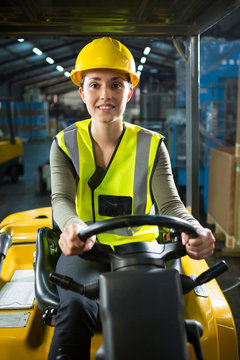 Beautiful female worker driving forklift in warehouse