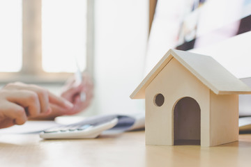 Wooden home model and key house on wood table with hand signing the document contract loan or...