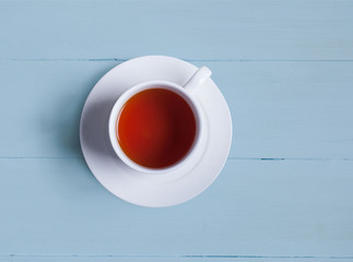 A cup of tea stands on the blue painted boards. View from above. A white cup and a white saucer.