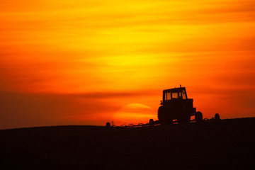 Tractor and cultivator silhouetted at sunrise