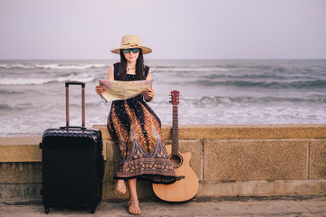 woman traveler looking for a map for find the way during vacation.Asia tourist have baggage and guitar sitting near the beach.