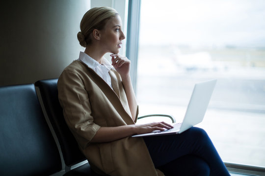 Thoughtful woman using laptop in waiting area