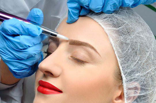 Microblading. Cosmetologist making permanent makeup. Attractive woman getting facial care and tattoo eyebrows