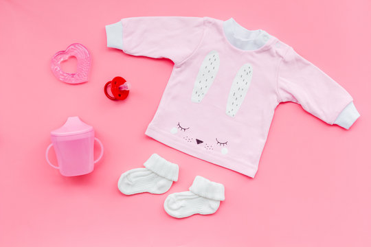 Newborn baby's background. Clothes for small girl with booties on pink background top view