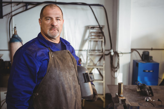 Welder holding welding helmet in workshop