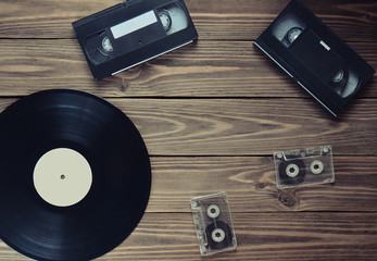 Vinyl record, video cassette, audio cassette on a  wooden background. Top view. Retro media...