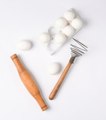 The cooking process. Plastic tray with white eggs, rolling pin, whisk on a white background. Top view..