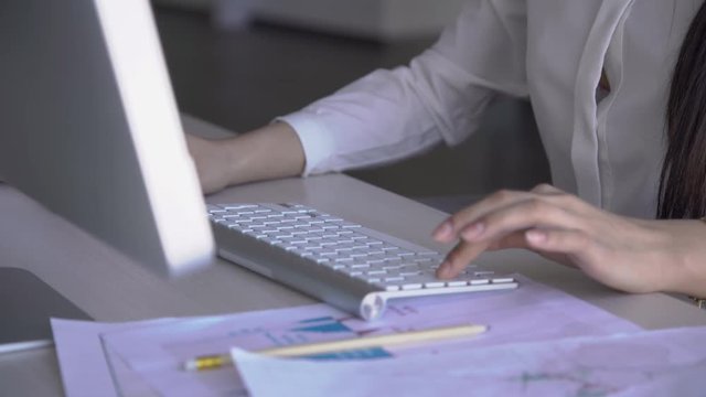 Woman typing text on white computer keyboard in office clothes among documents. Concept: female work, office style, typing keyboard