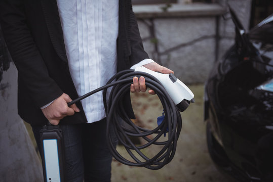 Woman holding car charger at electric vehicle charging station