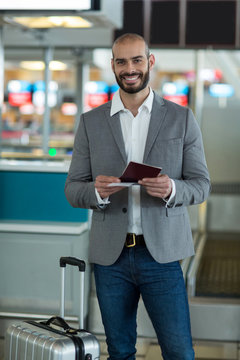 Portrait of smiling businessman with luggage checking his boarding pass