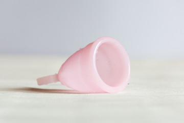 Pink menstrual cup lies on a white vintage wooden background. Selective focus, copy space