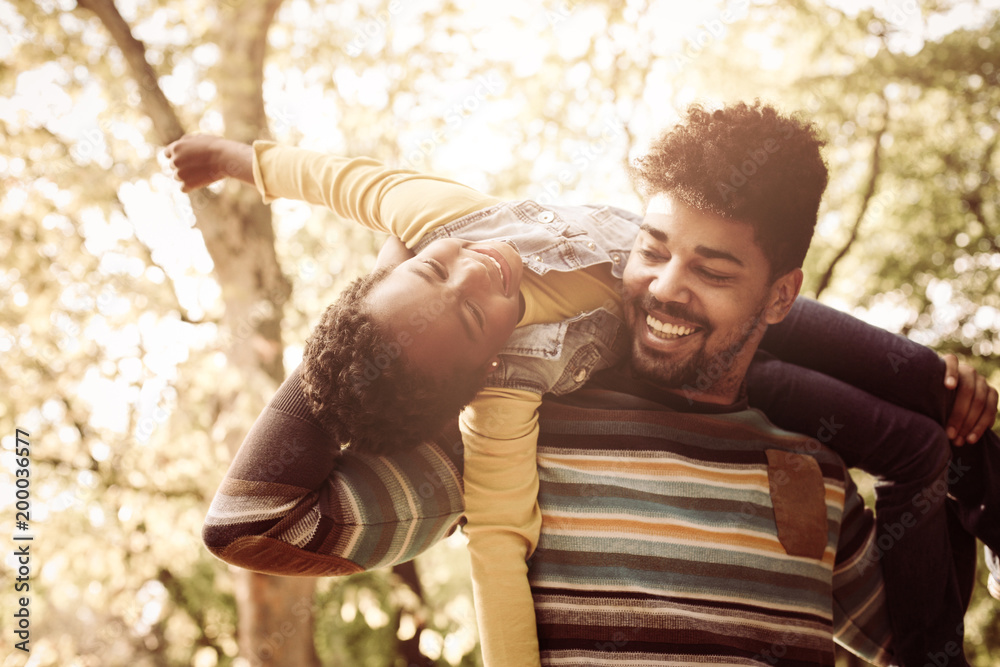 Sticker Happy African American father in park carrying his daughter on shoulders.