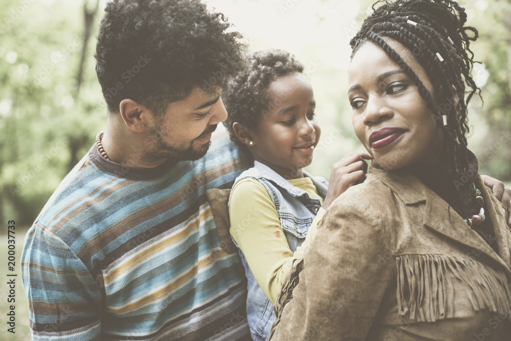 Wall mural Happy African American family enjoying in park and mother holding daughter on piggyback.