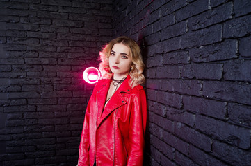 Studio portrait of blonde girl in red leather jacket against brick wall.