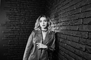 Studio portrait of blonde girl in red leather jacket against brick wall.