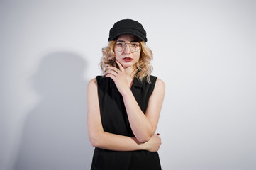 Studio portrait of blonde girl in black wear and cap against white background.