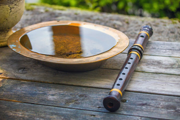 Indian flute on a table with ancient brass plate with water © Judita