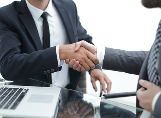 handshake business partners in front of the open laptop