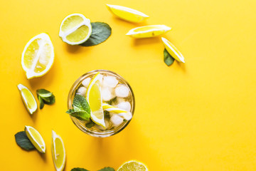Ice tea with ice, lemon and mint on a combined colored yellow background. Summer cold drink cocktail. Top view, flat lay