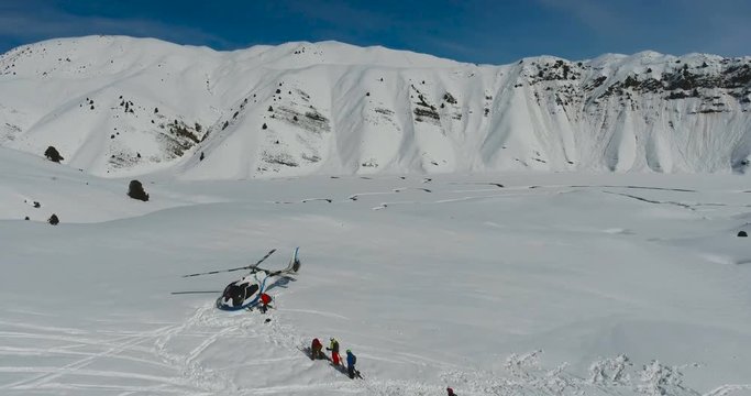 Skiers and snowboarders board a Helicopter in the winter mountains. Aerial view, camera move forward.