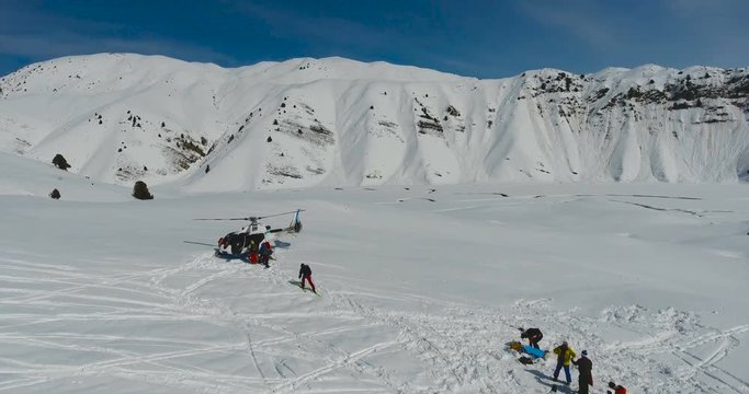 Skiers and snowboarders board a Helicopter in the winter mountains. Aerial view, camera slide down.