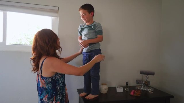 Mother and son horsing around in their bedroom with the son jumping onto the bed and his mom tickling him.