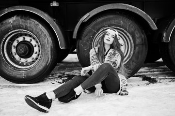 Brunette stylish casual girl in cap sitting against truck wheels.