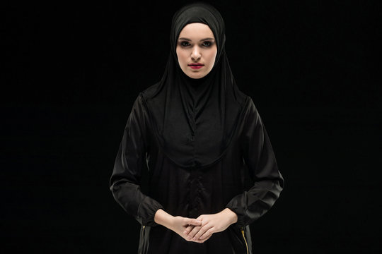 Beautiful young woman wearing black hijab as conservative fashion concept on black background holding hand on hand