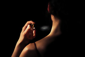 Woman sprays perfume on her neck with a black background