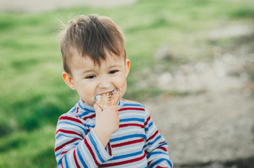little cute boy eating ice cream three years very appetizing, amid nature, green grass